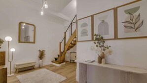 Ein modernes Interieur mit Treppe, Spiegel, gerahmten Kunstwerken und einem Konsolentisch mit Vasen.