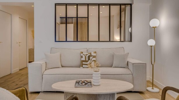 Ein Wohnzimmer mit einer Couch, einem runden Couchtisch, einer Stehlampe und einem großen Fenster mit Jalousien.