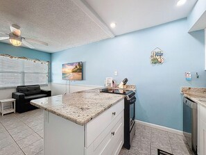 A modern kitchen with a granite countertop, a built-in oven, and a dining area with a black leather couch. - Harbor House 26 (Treasure Island)