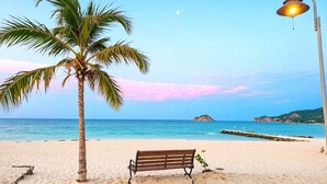 A beach with a palm tree, a bench, and a street lamp. - Reserva del Mar II Apartment - Cantamar SOHO -383A (Santa Marta)