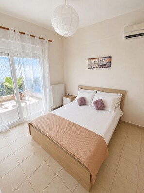 A bedroom with a bed, a nightstand, a window with curtains, a radiator, and a ceiling light.
