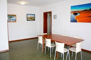 A dining area with a wooden table and white chairs, a clock on the wall, and two framed pictures. - Equipped Flat With Garden and Pool (Lignano Sabbiadoro)