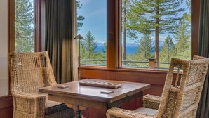 Une pièce avec une table en bois et des chaises en osier, de grandes fenêtres donnant sur des arbres et des montagnes.