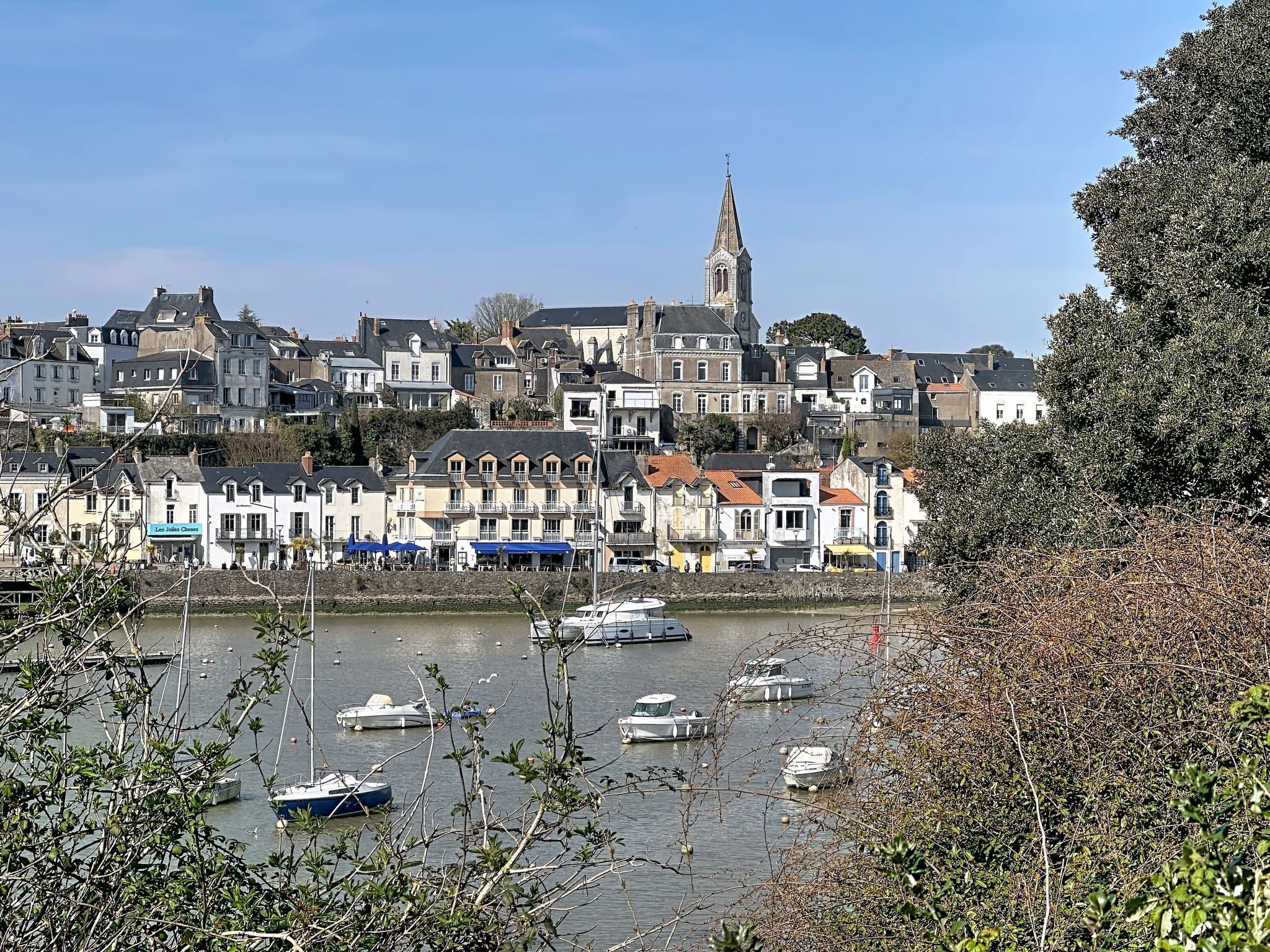 A coastal town with historic buildings, a prominent church tower, and boats docked along the waterfront.