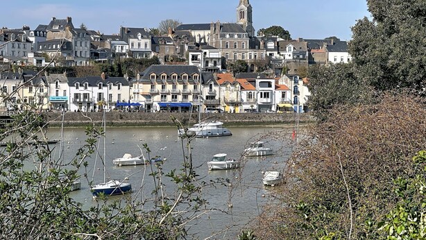 Une ville côtière dotée de bâtiments historiques, d’un clocher d’église imposant et de bateaux amarrés le long du quai.