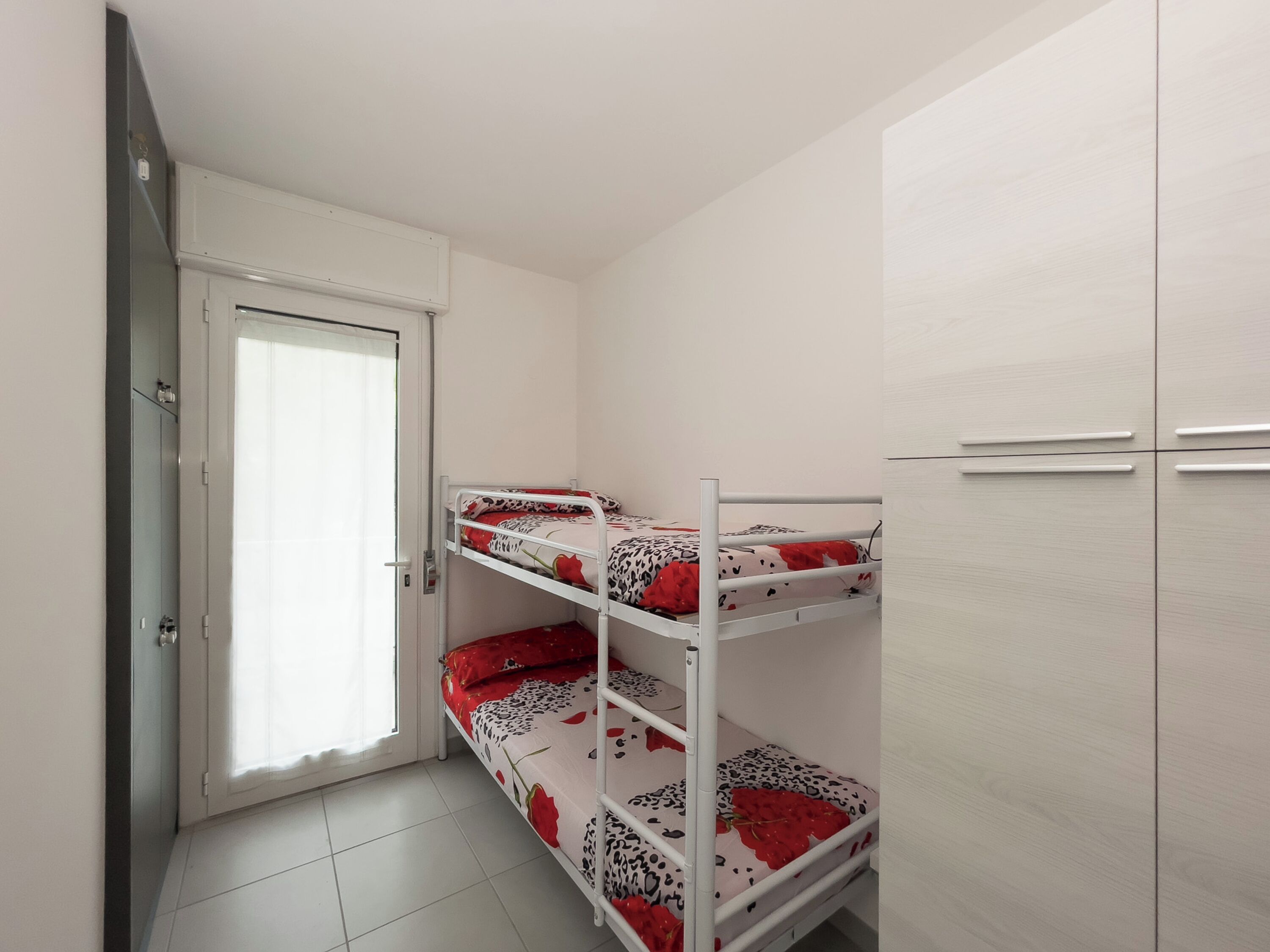 Une chambre avec des lits superposés, une armoire et une porte avec une fenêtre.