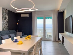 Ein modernes Wohnzimmer mit Essbereich, einer Couch, einem Fernseher und einem Balkon mit Blick.