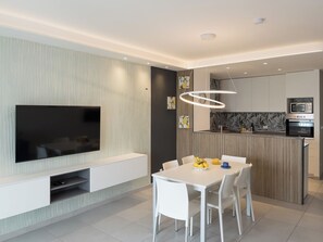 A modern kitchen with built-in appliances, a dining area with a white table and chairs, and a mounted flat-screen TV. - Modern Vacation Home With a sea View Balcony (Lignano Sabbiadoro)
