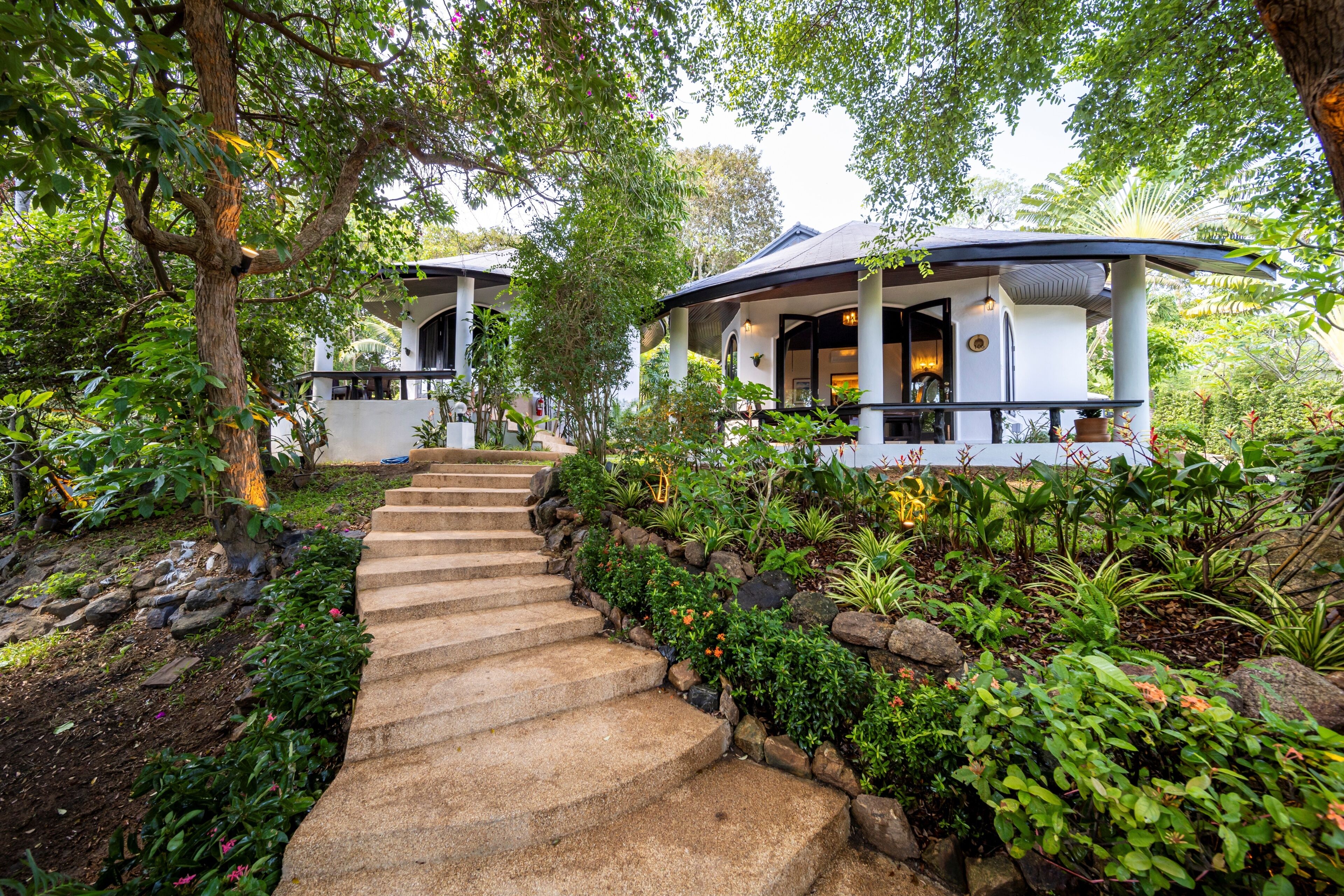 A pathway leading to a building with a covered porch, surrounded by lush greenery and a stone staircase.