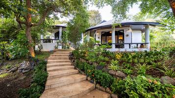 A pathway leading to a building with a covered porch, surrounded by lush greenery and a stone staircase.