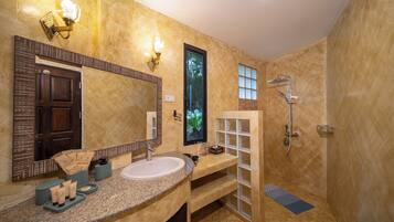 A bathroom with a granite countertop, a large mirror, a shower, and a window with a view of greenery.