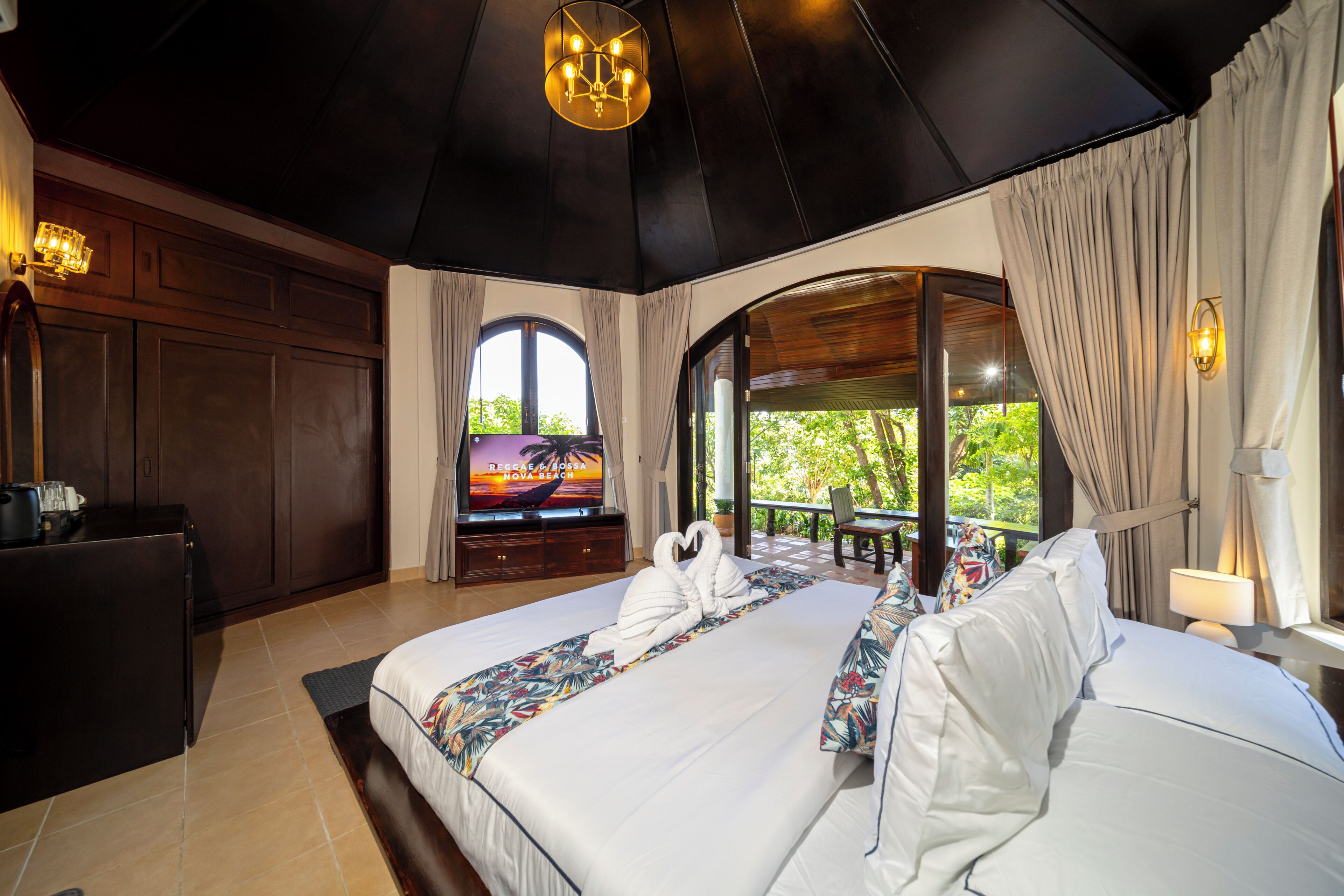 A hotel room with a large bed, a TV, a desk, and a view of greenery.