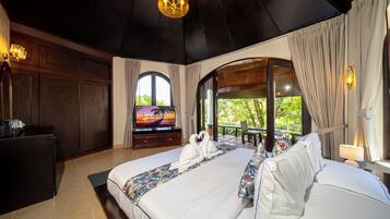 A hotel room with a large bed, a TV, a desk, and a view of greenery.