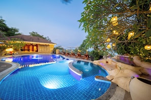A swimming pool with a tiled edge, surrounded by lounge chairs and a building with a thatched roof. - Luxury Cottage, Balcony, Garden View (Koh Samui)
