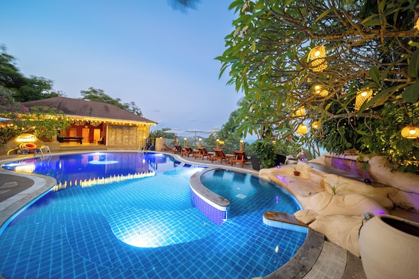 A swimming pool with a tiled edge, surrounded by lounge chairs and a building with a thatched roof. - Luxury Cottage, Balcony, Garden View (Koh Samui)