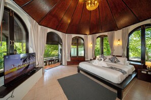 A bedroom with a large bed, a TV, and a view of the outdoors. - Luxury Cottage, Balcony, Garden View (Koh Samui)