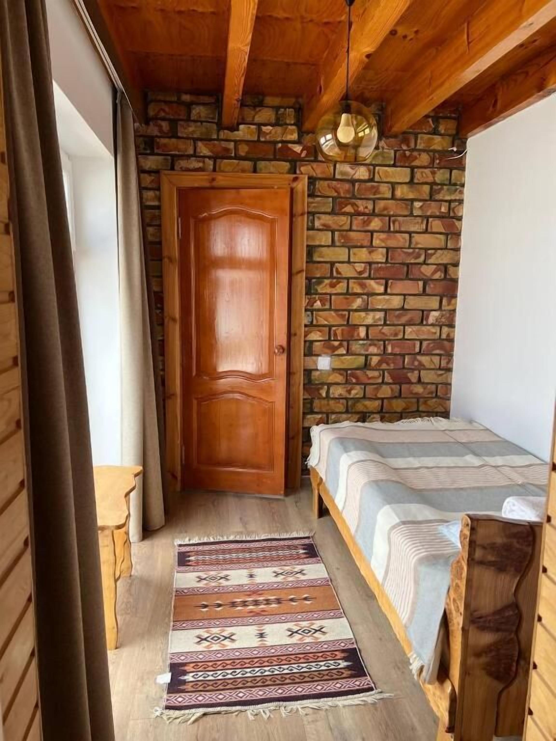Ein kleines, gemütliches Zimmer mit Holztür, einem Bett mit gestreifter Bettdecke und einem gemusterten Teppich.
