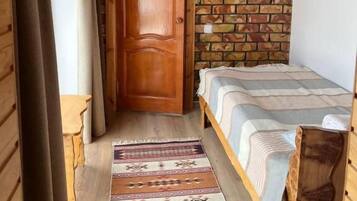 Ein kleines, gemütliches Zimmer mit Holztür, einem Bett mit gestreifter Bettdecke und einem gemusterten Teppich.
