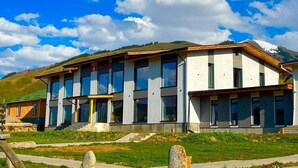 A modern building with large windows and a flat roof, surrounded by greenery and hills. - Kemin Guest House (Kaindy)