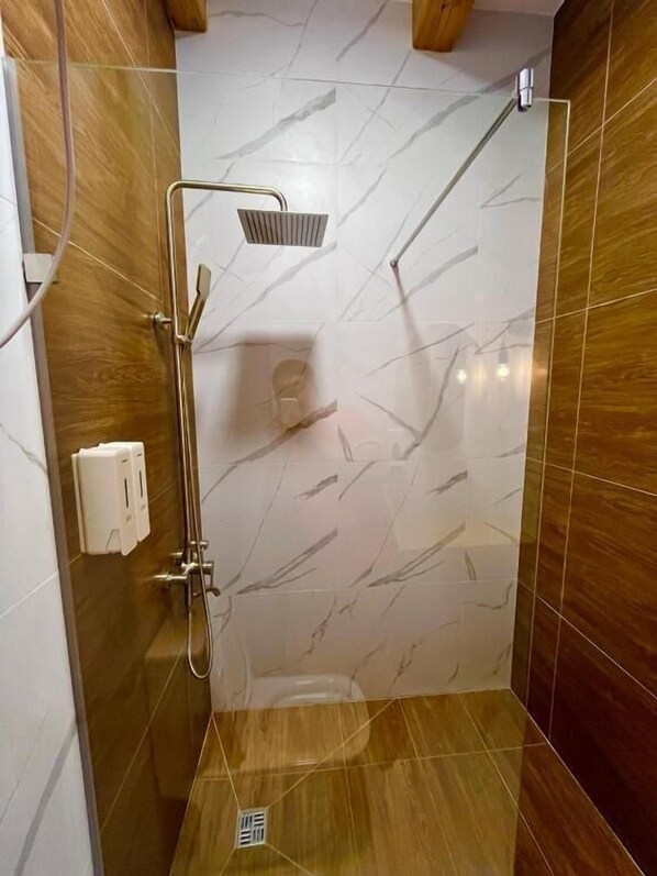 Una ducha con cabezal de ducha de mano, grifo empotrado y dispensador de jabón.