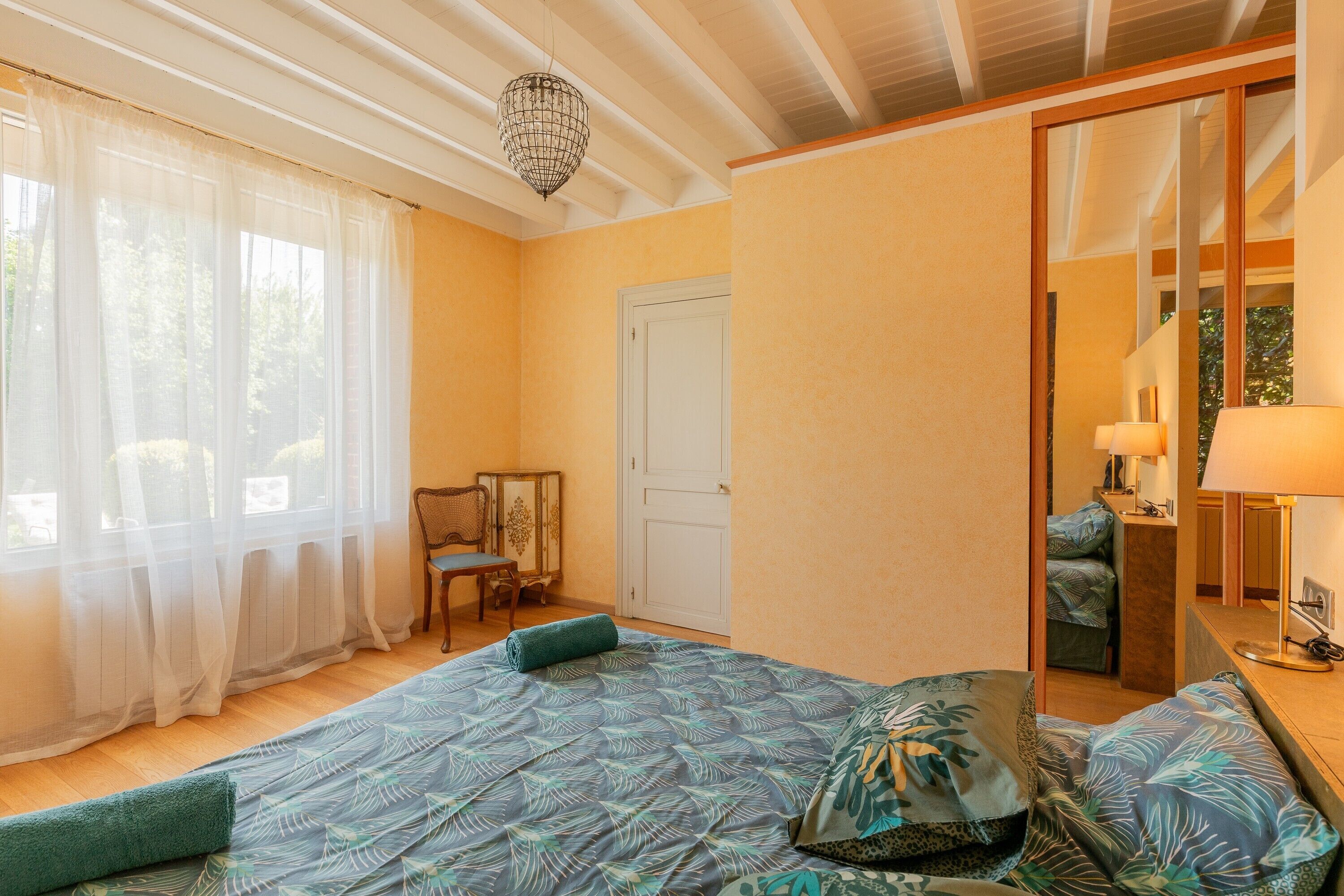 A bedroom with a bed, a chair, a desk, and a mirror.