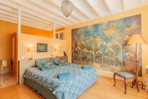 Ein Schlafzimmer mit einem Bett, einem Sessel, einer Lampe, einem Gemälde und einer Deckenleuchte.