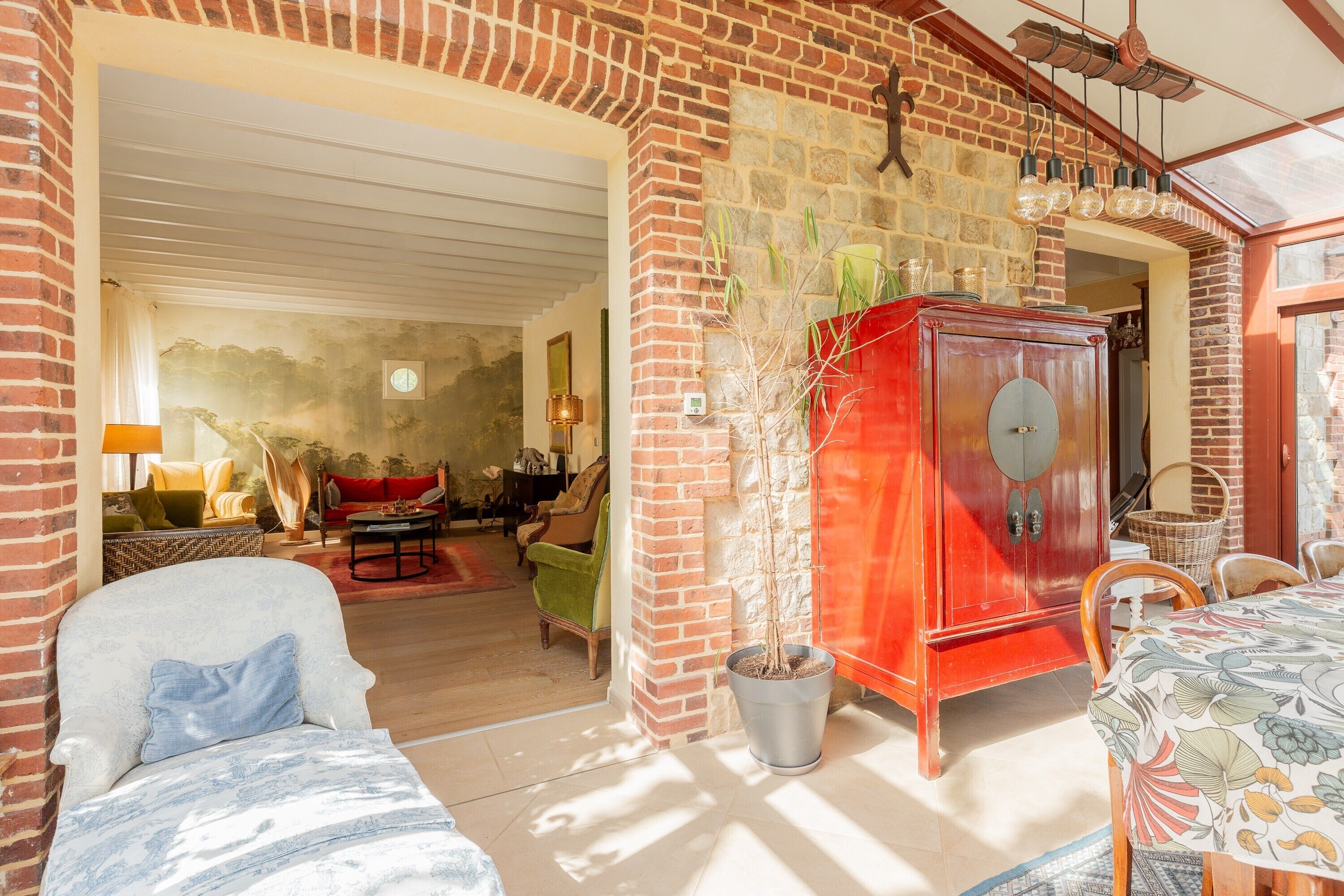 Ein Zimmer mit Backsteinwand, Holzschrank, Esstisch mit Stühlen, einer Couch und einem Blumentopf.