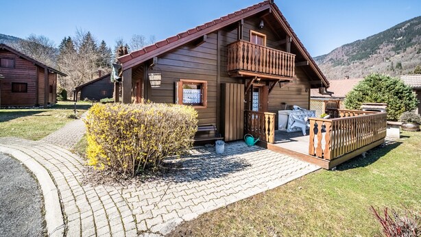 Eine Holzhütte mit Balkon, gepflastertem Zugang und einer umliegenden Naturlandschaft.