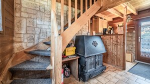 Eine Holztreppe führt zu einer Steinwand, ein schwarzer Holzofen und ein Küchenbereich mit Holzausbau und einem Fenster.