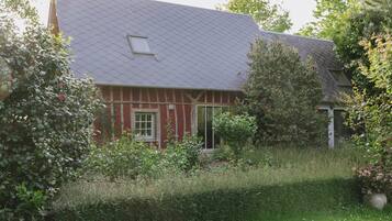 Una casa con fachada roja, techo gris y un jardín con diversas plantas y un jarrón grande.