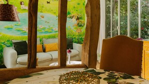 Une chambre avec une tête de lit en bois, une nappe à motifs floraux, un bol décoratif et une fresque représentant un jardin.