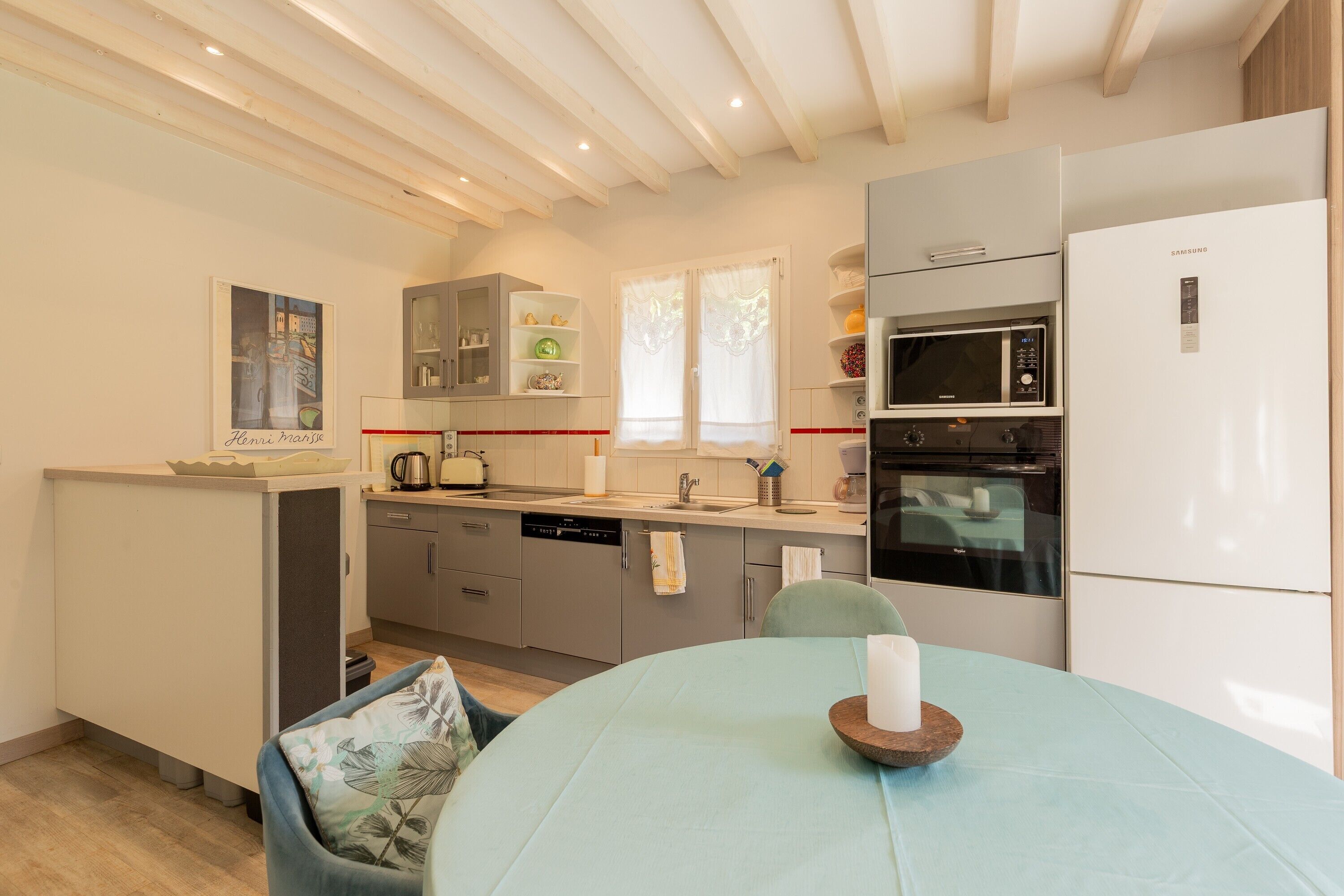 A compact kitchen with modern appliances, a dining area with a table and chairs, and a small cabinet with decorative items.