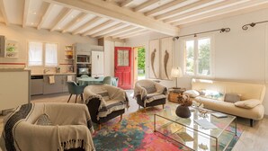 A spacious living area with a sofa, armchairs, a glass coffee table, and a kitchen in the background. - La Maison des Mésanges: Private Terrace, Wi-Fi, Reversible Heat Pump, Artist's Garden (La Chapelle-sur-Dun)