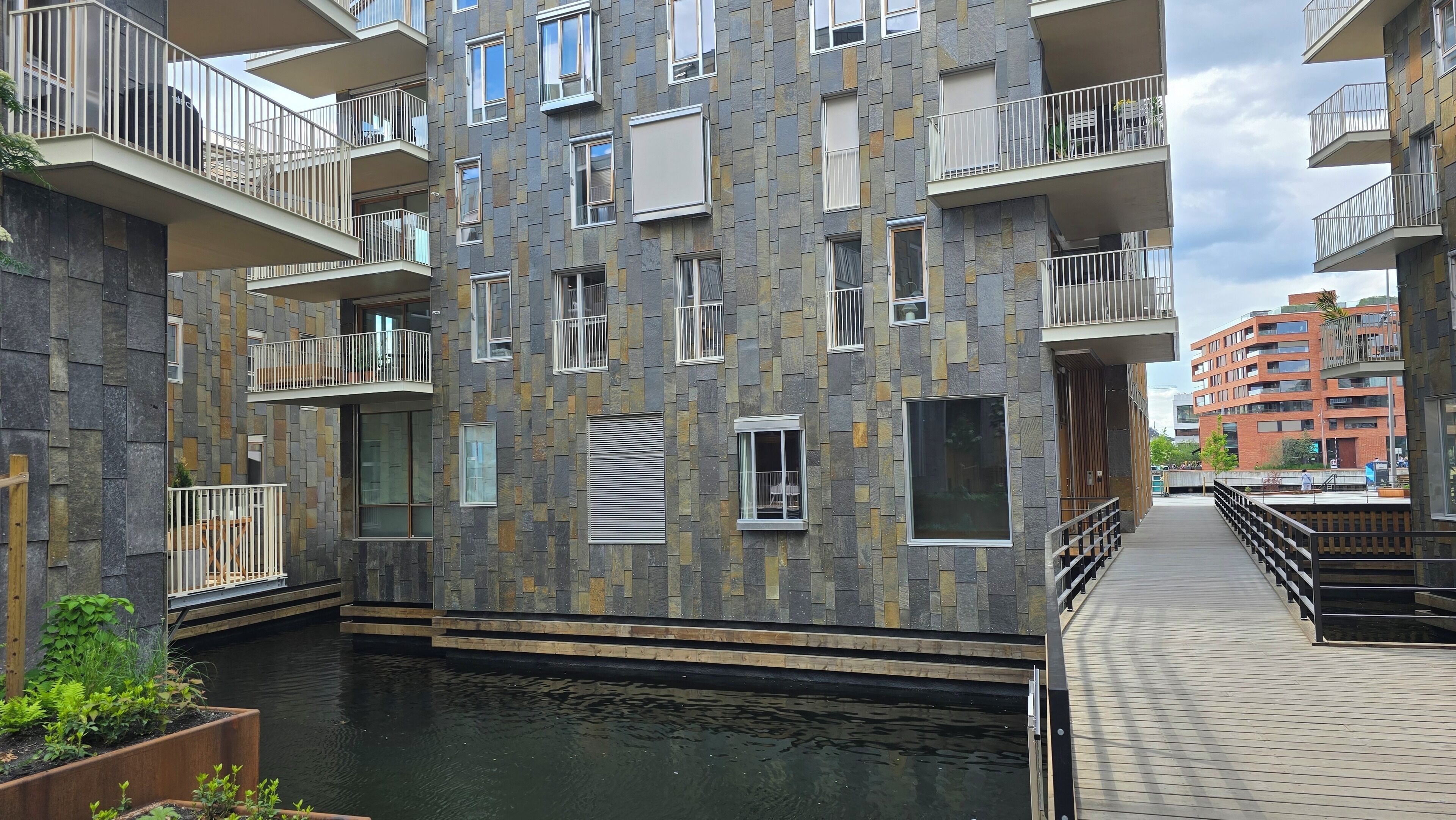 A multi-story residential building with balconies, a water feature, and a wooden deck.
