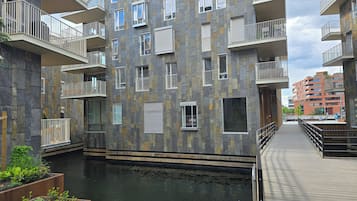 A multi-story residential building with balconies, a water feature, and a wooden deck.