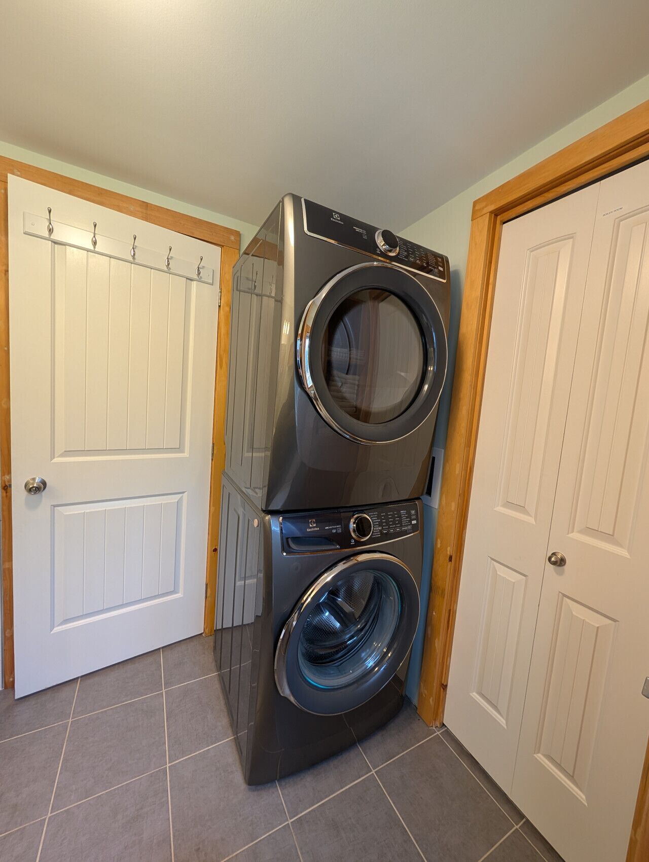 A stacked washer and dryer in a room with white doors and tiled flooring.