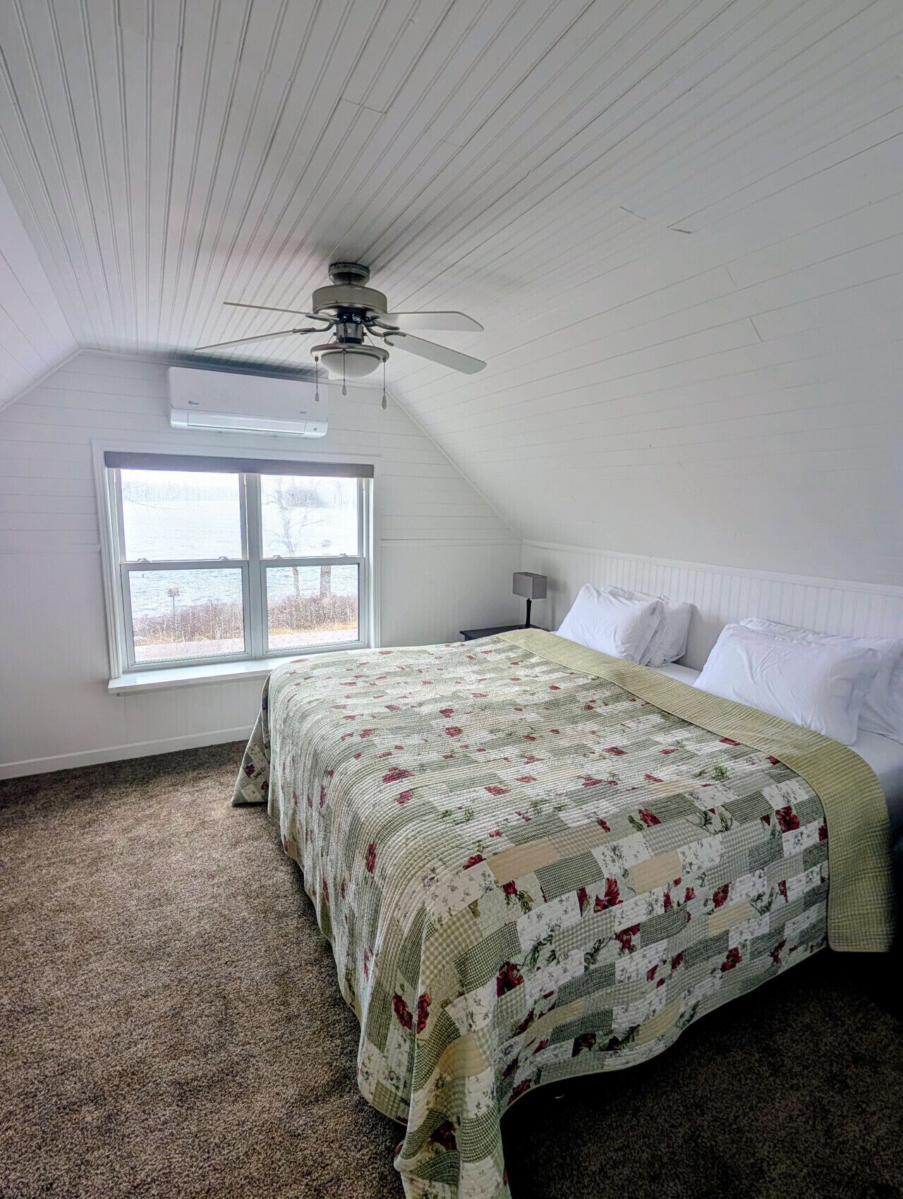 A bedroom with a bed, a ceiling fan, a window, and an air conditioning unit.