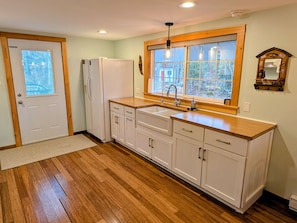 A kitchen with wooden flooring, white cabinets, a double sink, and a window with a view.