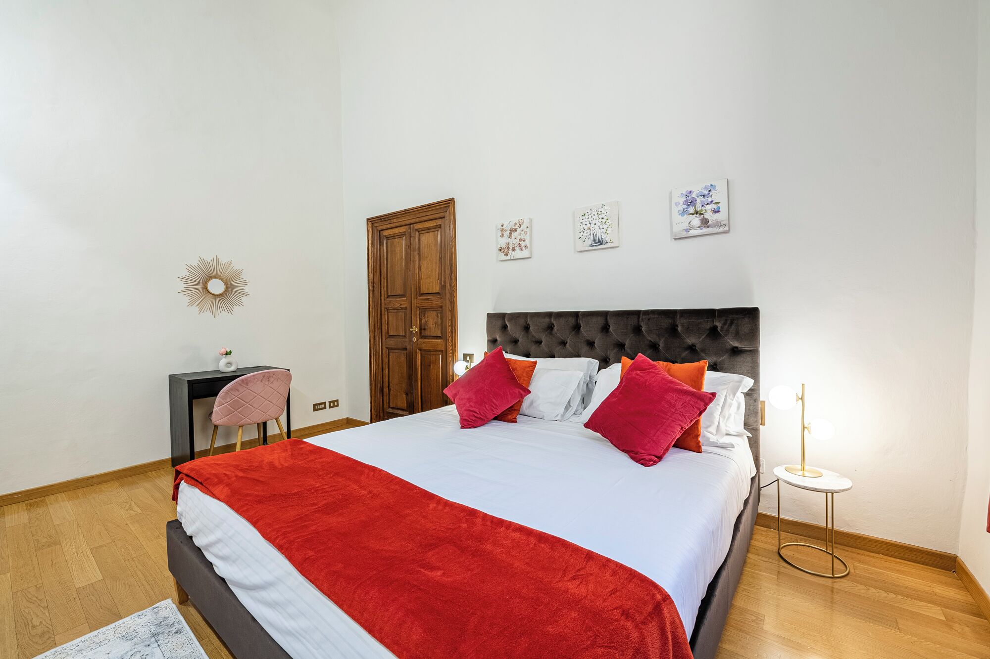 A bedroom with a bed, a desk, a chair, a door, and wall art.