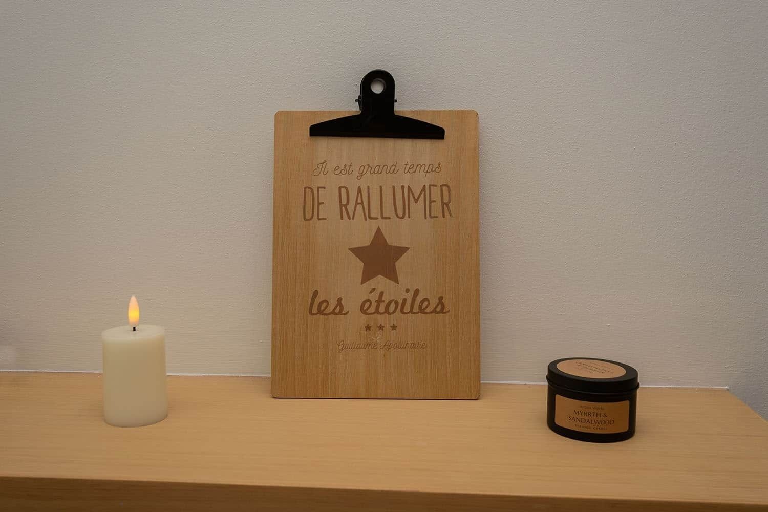 A wooden board with text and a candle, and a jar of scented wax on a shelf.