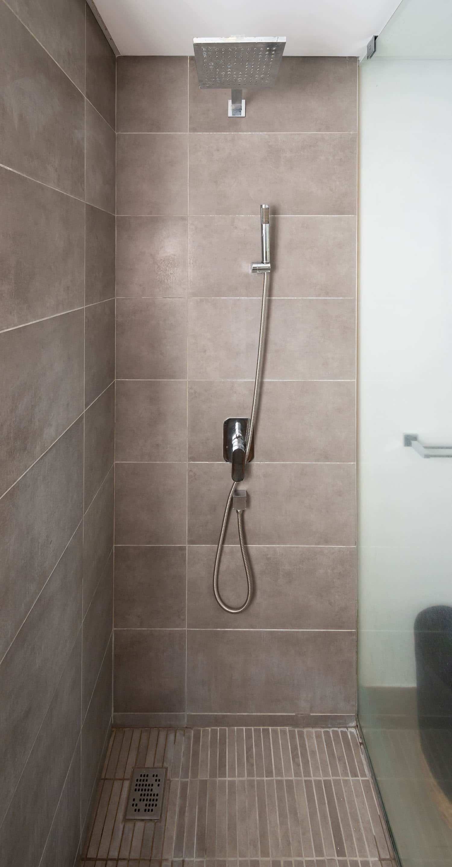 A shower with a handheld showerhead and a wall-mounted faucet.