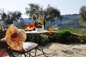 Un espace de restauration en plein air avec une table dressée pour deux personnes, une bouteille de vin et un bol d’olives.