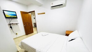 A bedroom with a bed, a TV, an air conditioner, and a door.