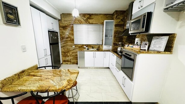A compact kitchen with white cabinets, a granite countertop, a built-in microwave, and a refrigerator.