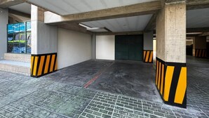 An indoor parking area with concrete pillars, a tiled floor, and a green door.