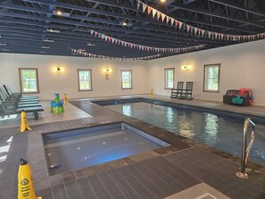 Indendørs swimmingpool med siddepladser, sikkerhedsskilte og et loft med spærkonstruktion.