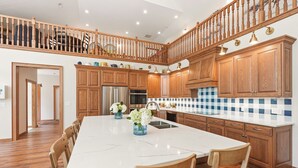 A spacious kitchen with wooden cabinets, a marble island, and a dining area with wooden chairs.