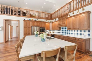 A spacious kitchen with wooden cabinets, a marble island, and a dining area with wooden chairs.