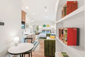 A modern, compact room with a kitchen, dining area, and a bed with a green upholstered headboard.