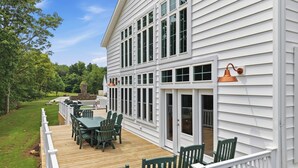 A covered deck with a table and chairs, a white house with green shutters, and a clear sky.